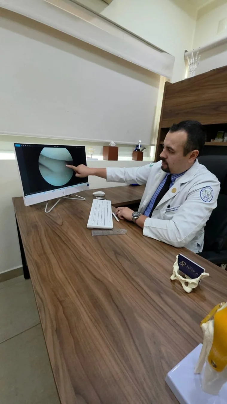 El Dr. Alan Polanco señala una imagen artroscópica de rodilla en el monitor.