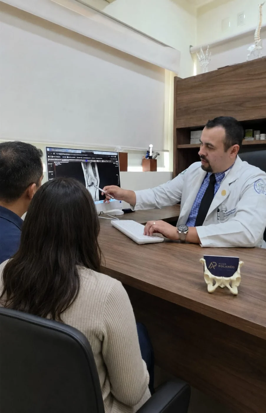 El Dr. Alan Polanco revisa un estudio de imagen de rodilla con pacientes en su consultorio.