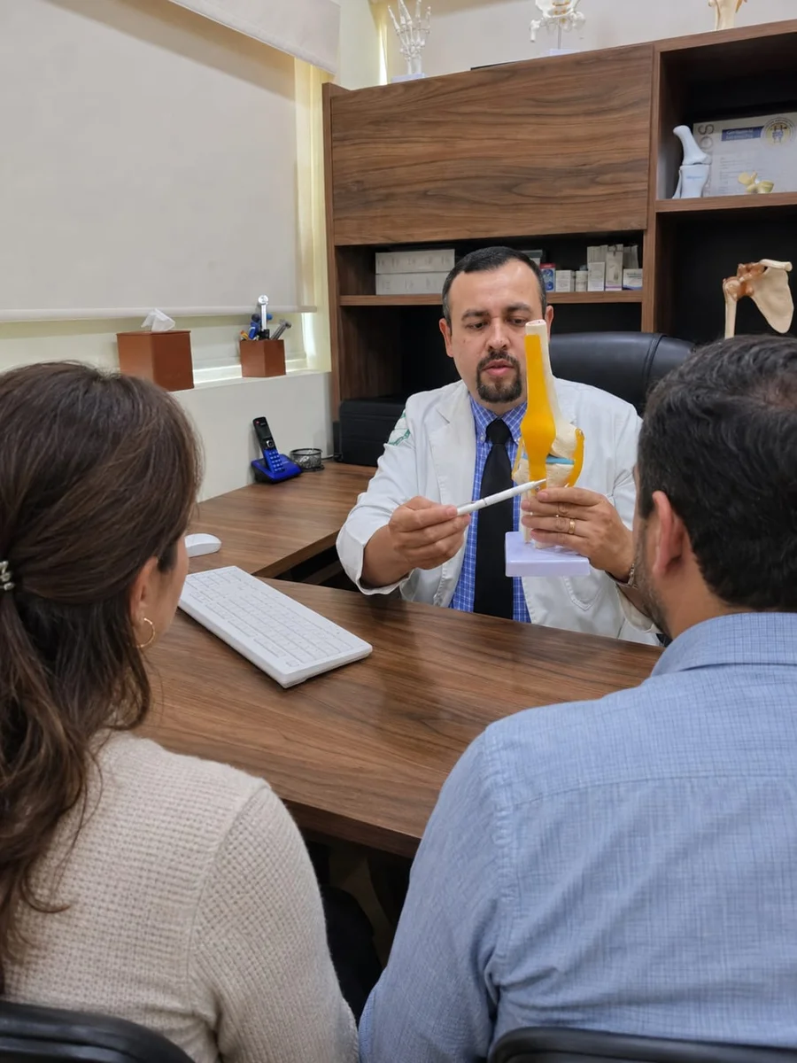 El Dr. Alan Polanco explica la anatomía de la rodilla a una pareja durante la consulta.